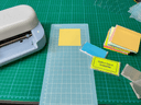 A Cricut Joy beside stacks of coloured Post-it notes and two clear printed note holders, one labelled GunPLA Tools & Accessories