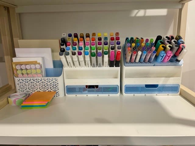 Two printed desk organisers with pull-out drawers, holding rows of alcohol markers beside a card holder and washi tape